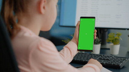 Naklejka premium Close up of child holding green screen on smartphone for homework and school tasks. Young girl looking at display with mockup template and isolated background for remote education.