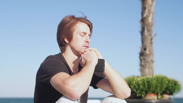 red-haired guy in a black T-shirt sits on the background of sea and blue sky