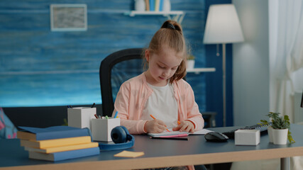 Fototapeta na wymiar Little child drawing with colorful pencils on notebook at desk for school task and homework. Young girl using supplies to draw on textbook for entertainment and fun after online class.