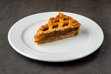 Delicious apple pie on a white porcelain plate on a dark stone background