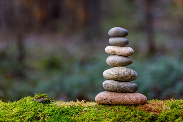 Pyramid stones balance on old mossy fallen tree. Stone pyramid in focus. Forest background blurred