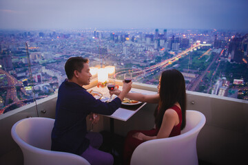 A young couple clinking wine glasses at a romantic dinner on the rooftop at night.