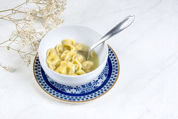 View of an agnoline soup dish with light background and flowers around