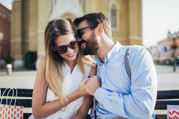 Portrait of beautiful smiling young couple sitting on a bench after shopping.