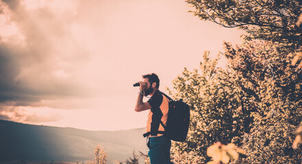 handsome man trekking in nature in autumn using binoculars slow travel
