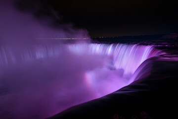 Niagara Falls illuminated in purple light with rainbows from the mist, Canada.