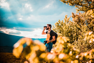 handsome man trekking in nature using binoculars slow travel
