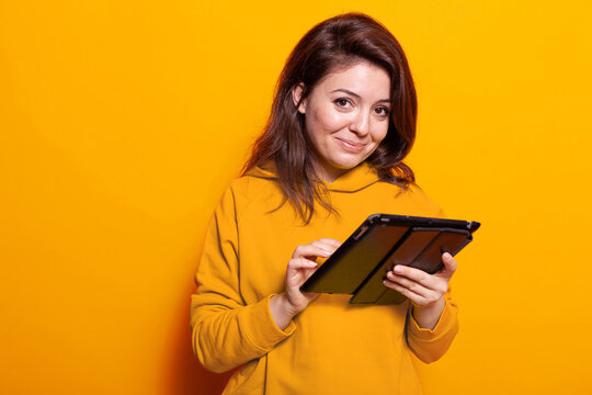 Caucasian adult using digital tablet with touch screen in studio. Cheerful woman holding modern gadget and looking at camera to work on online internet connection. adult with device