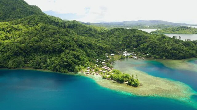 Aerial view of flying away from a tropical coastal village and it's harbour and surrounding reefs.