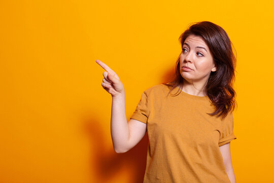 Caucasian person indicating finger at left side of studio while posing for pictures and photography. Cheerful woman looking aside while doing gesture and sign with hand over background.