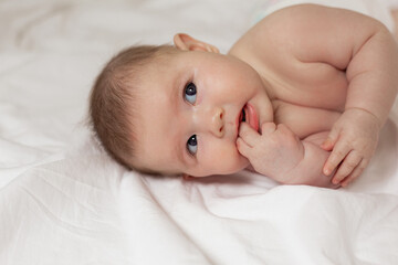 cute thoughtful newborn baby is lying on its side on a white bed. products for children. concept of a happy childhood and motherhood. child care. space for text. High quality photo