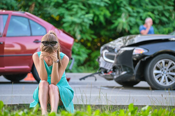 Sad female driver sitting on street side shocked after car accident. Road safety and vehicle...