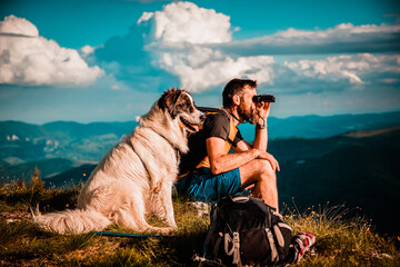 handsome man and white dog trekking in nature using binoculars slow travel