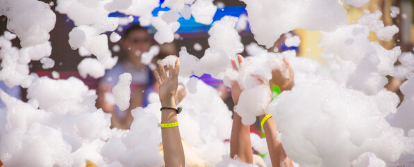 Foam party entertainment, people have fun raising hands catch soap bubbles, summer entertainment...