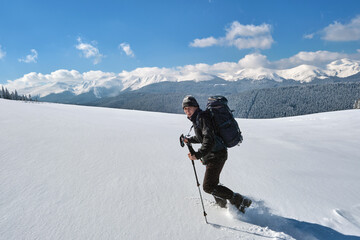 Naklejka na ściany i meble Man backpacker hiking snowy mountain hillside on cold winter day.