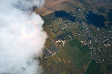 Aerial view from airplane window at high altitude of distant city covered with puffy cumulus clouds...