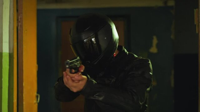 Trained army man in protective moto helmet with handgun walking carefully along demolished abandoned building room close view slow motion