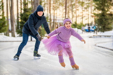 little girl in pink sweater and full skirt rides on sunny winter day on an outdoor ice rink in park
