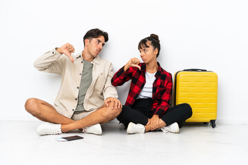 Obraz premium Young mixed race travelers couple sitting on the floor isolated on white background showing thumb down sign with negative expression