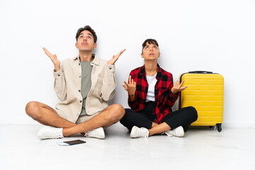 Obraz premium Young mixed race travelers couple sitting on the floor isolated on white background frustrated by a bad situation