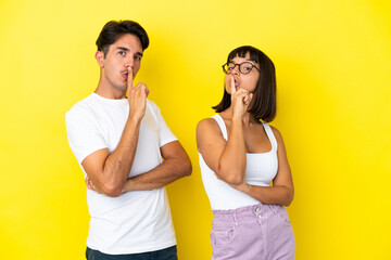 Young mixed race couple isolated on yellow background showing a sign of closing mouth and silence gesture