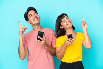 Young mixed race couple holding mobile phone isolated on blue background pointing with the index finger a great idea