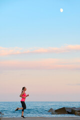 young woman running on city promenade at sunset with visible moon