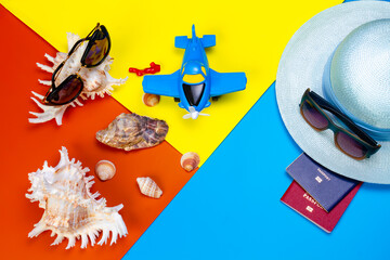 Beach accessories with sunglasses, passports, straw hat, flip-flops, seashells and a toy airplane on a colored background. Summer vacation. Summer background.