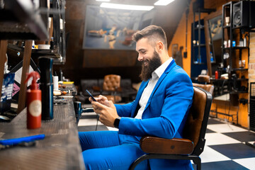 Male businessman in a suit using a smartphone in a hair salon