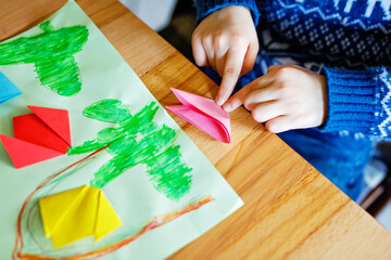 Closeup of hands of little kid making tulip flowers origami for a postcard for mother's day or birthday.