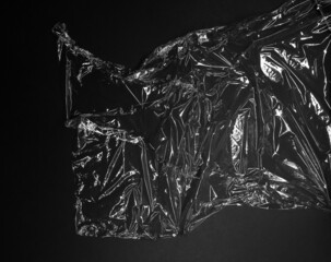 Reflecting light and shadow on creases and folds in scrunched clear plastic foil on black background