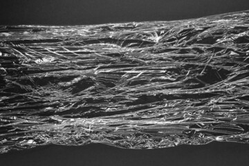 Reflecting light and shadow on creases and folds in scrunched clear plastic foil on black background