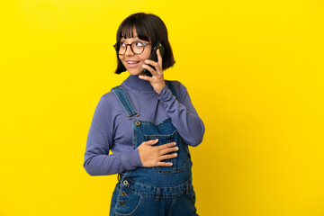 Young pregnant woman over isolated yellow background keeping a conversation with the mobile phone with someone