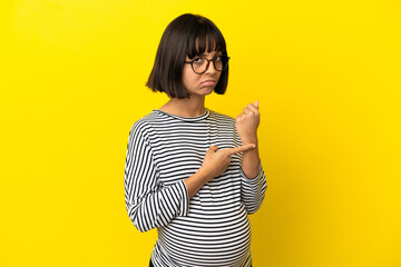 Young pregnant woman over isolated yellow background making the gesture of being late