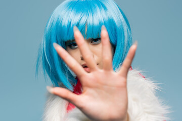 Asian woman in wig pulling hand at camera isolated on blue