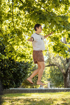 Mujer joven en un parque con los brazos estirados caminando sobre una cuerda de equilibrismo. Deportes al aire libre, concepto.