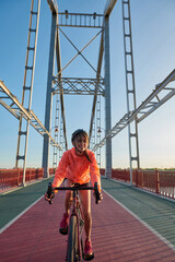 Smiling millennial girl ride bike on city bridge