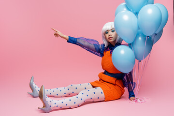 Asian pop art model pointing with finger near blue balloons on pink background