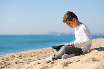 Naklejka na ściany i meble Little kid reading a book on the beach