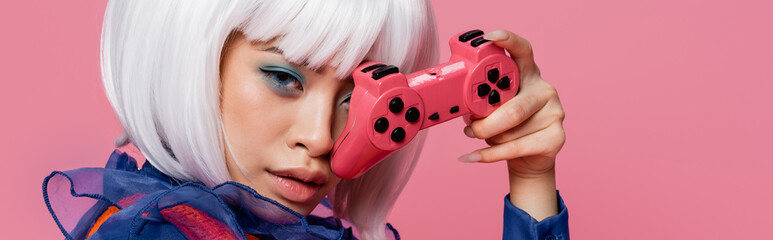 KYIV, UKRAINE - DECEMBER 10, 2020: Asian pop art woman in white wig holding joystick isolated on pink, banner