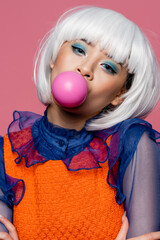 Asian model in pop art style blowing bubble gum isolated on pink