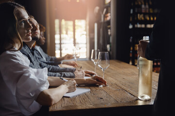 Closeup hand of man open bottle of white wine and sommelier making notes at degustation card