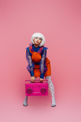 Young asian pop art woman in dotted tights holding boombox on pink background