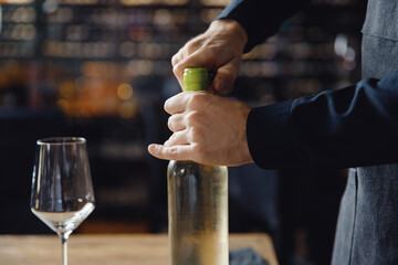 Closeup hand of Sommelier opens cork of bottle of white wine with corkscrew