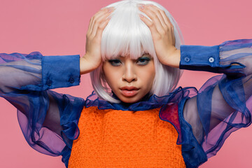 Asian pop art model holding hands near head and looking at camera isolated on pink