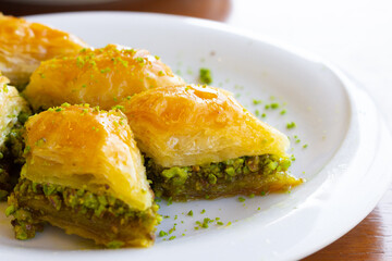 A close-up shot of Turkish dessert baklava slices on a white plate. Selective focus on foreground.