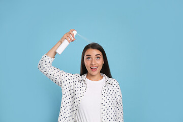 Young woman applying dry shampoo against light blue background