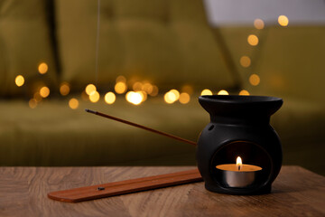 Black aroma lamp,candle flame and incense sticks against cozy warm lights on the home sofa.Empty...