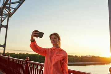 Smiling sporty girl take selfie on cellphone training outdoors