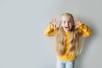 Studio shot of emotional adorable Caucasian little girl raising eyebrows and open mouth with tongue, hand being surprised and shocked, showing true astonished reaction on unexpected news